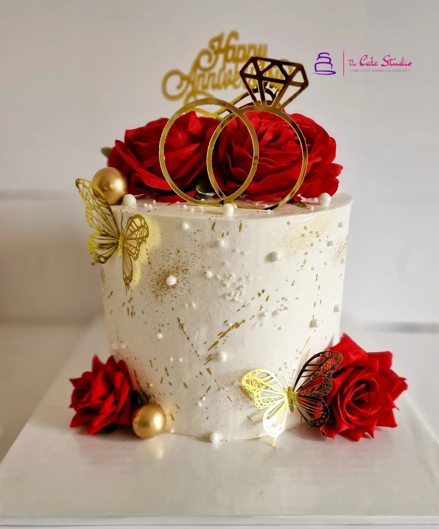 A romantic two-tier anniversary cake with white fondant, sugar peonies, and a gold acrylic topper, by The Cake Studio Harare