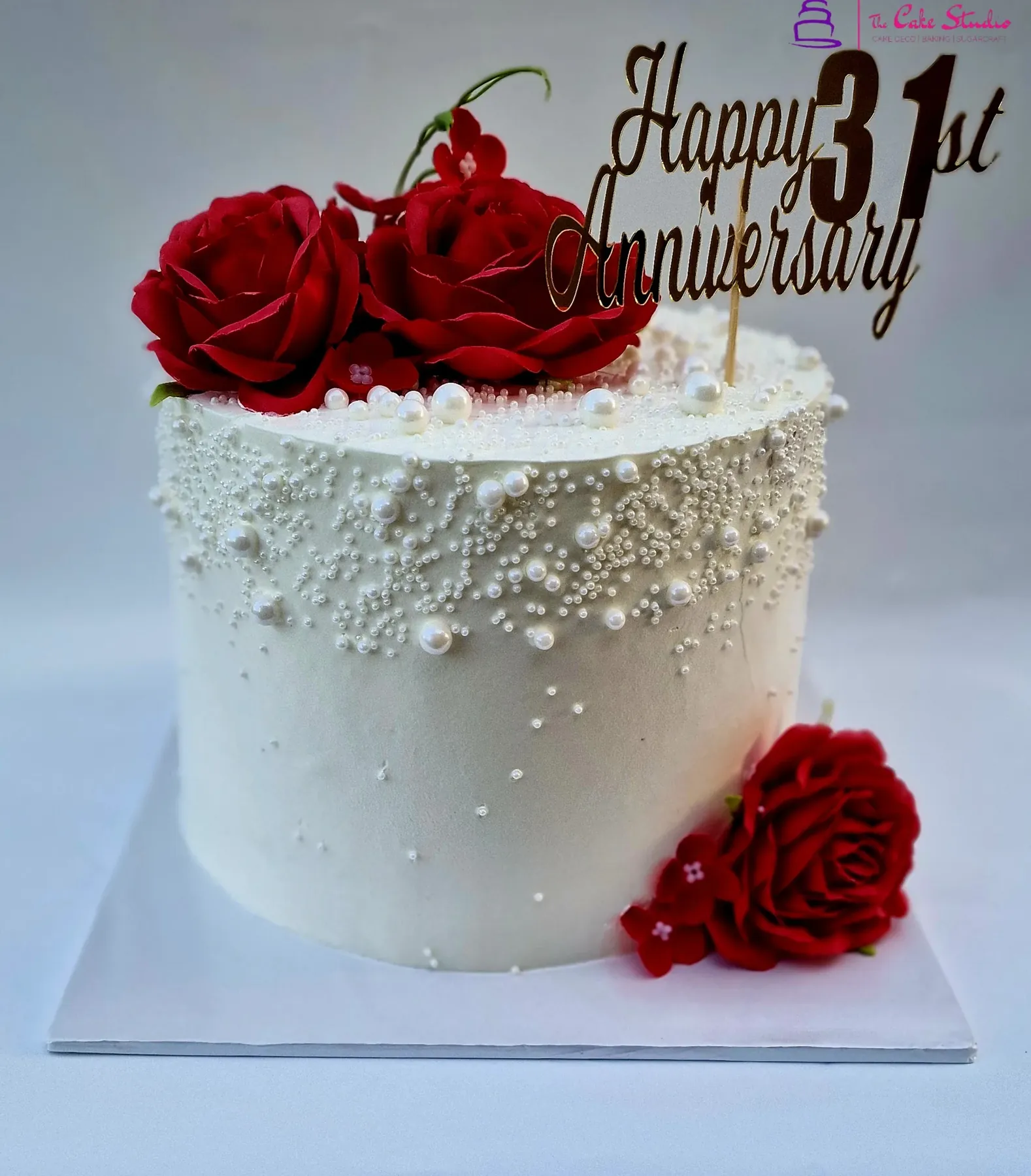 A 31st anniversary cake with white pearl detail, fresh red roses, and a gold "Happy 31st Anniversary" topper, by The Cake Studio Harare