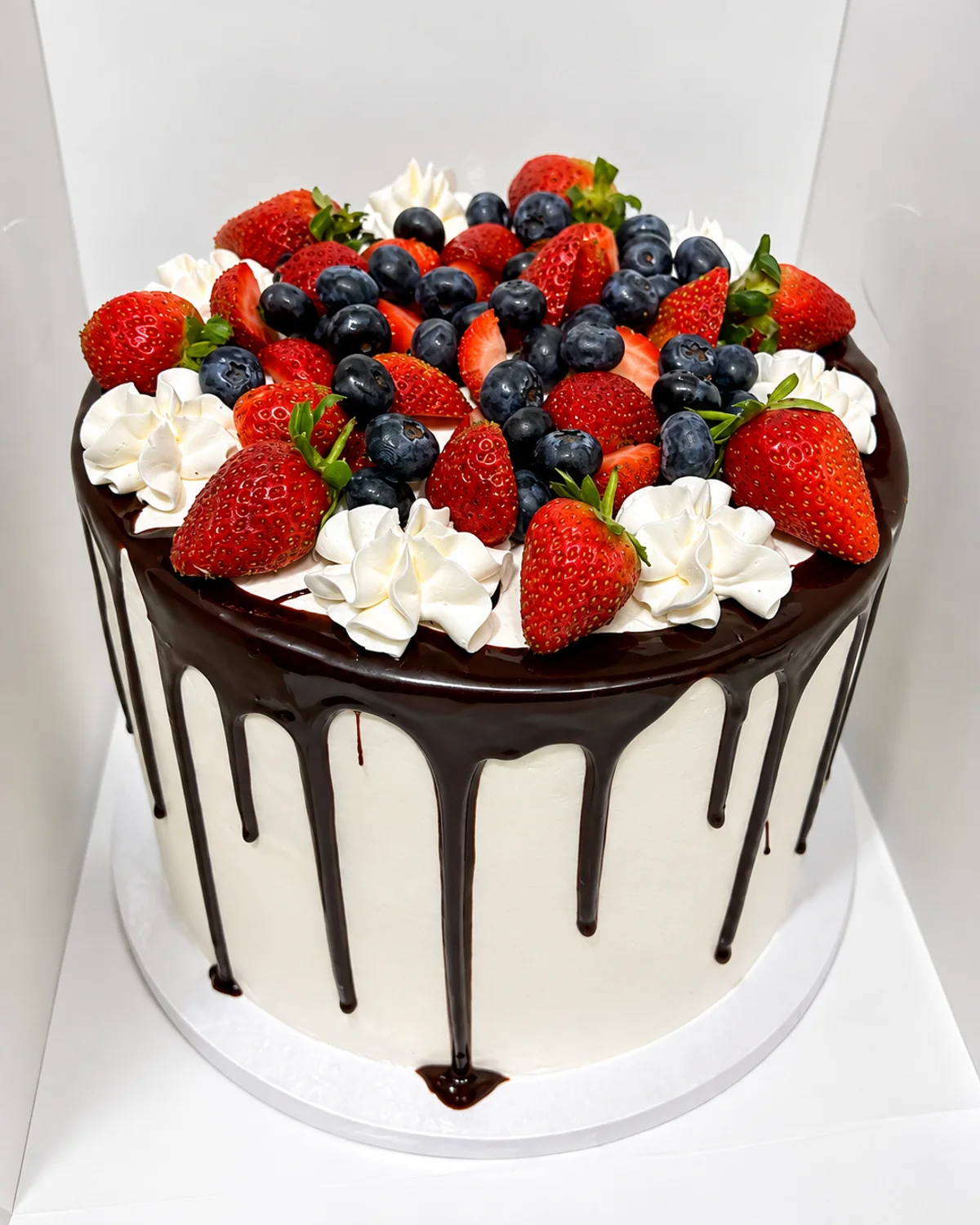 A Black Forest cake finished in fresh cream with a dark chocolate drip, topped with strawberries and blueberries, baked by The Cake Studio Harare