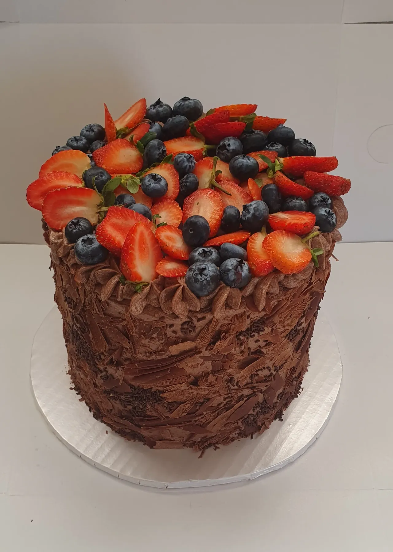 A Black Forest cake topped with fresh strawberries and blueberries on chocolate buttercream, baked by The Cake Studio Harare