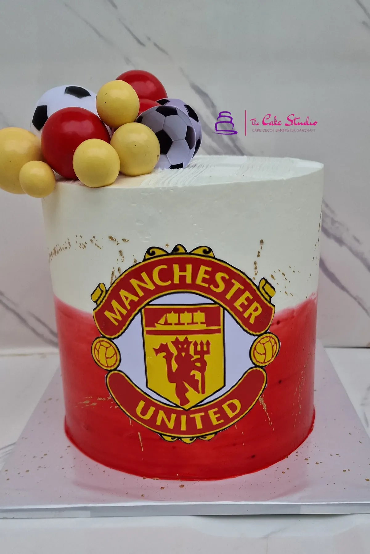 A Manchester United themed cake with sugar-ball footballs in club colours, baked by The Cake Studio Harare