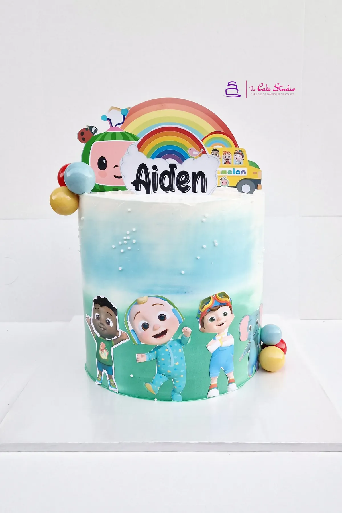 A Cocomelon themed character cake with hand-painted scene, rainbow topper, and a personalised name plaque, baked by The Cake Studio Harare