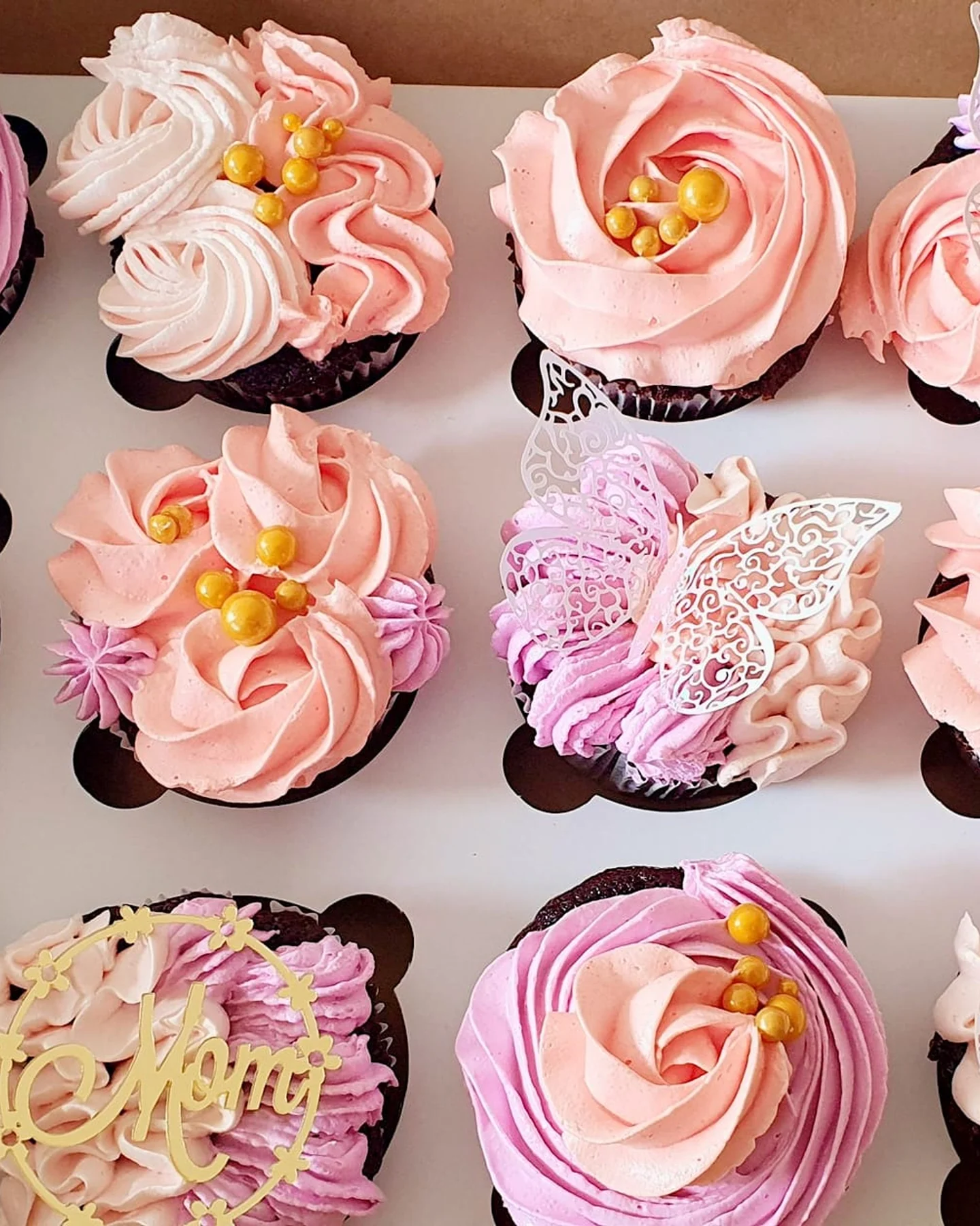 A presentation box of pink and peach buttercream cupcakes with butterfly toppers and personalised acrylics, by The Cake Studio Harare