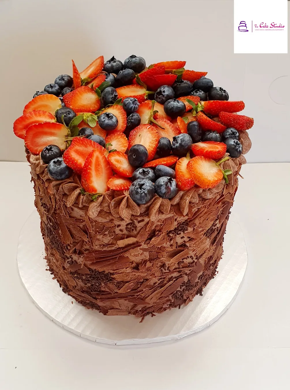 A chocolate cake piled with strawberries and blueberries