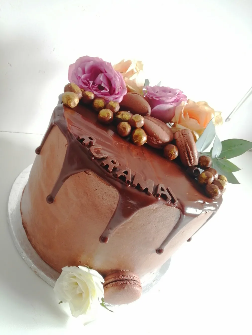 A chocolate drip cake with gold-dusted chocolate eggs, chocolate macarons, roses and a chocolate name plaque, by The Cake Studio Harare