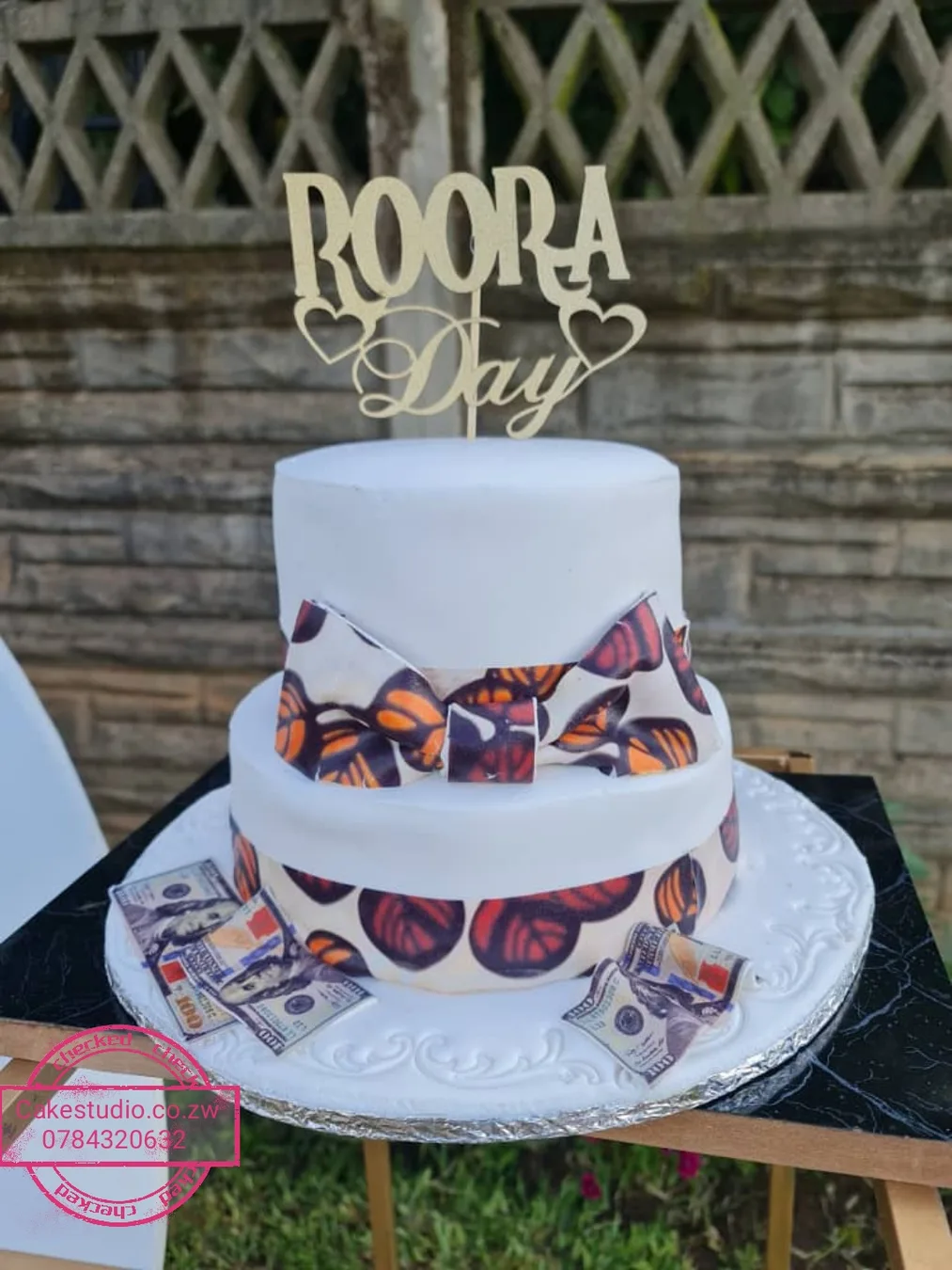 A two-tier white Roora Day cake with a gold Roora Day topper