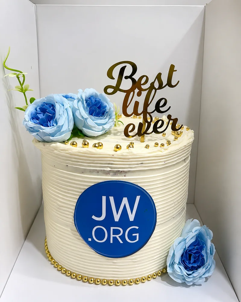 A red velvet celebration cake in textured cream frosting with gold pearl borders, soft blue roses and a gold Best life ever topper, by The Cake Studio Harare