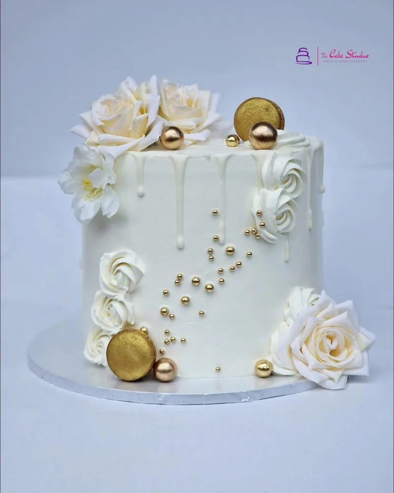 A white and gold celebration cake with clean tiers and gold detailing, made by The Cake Studio Harare