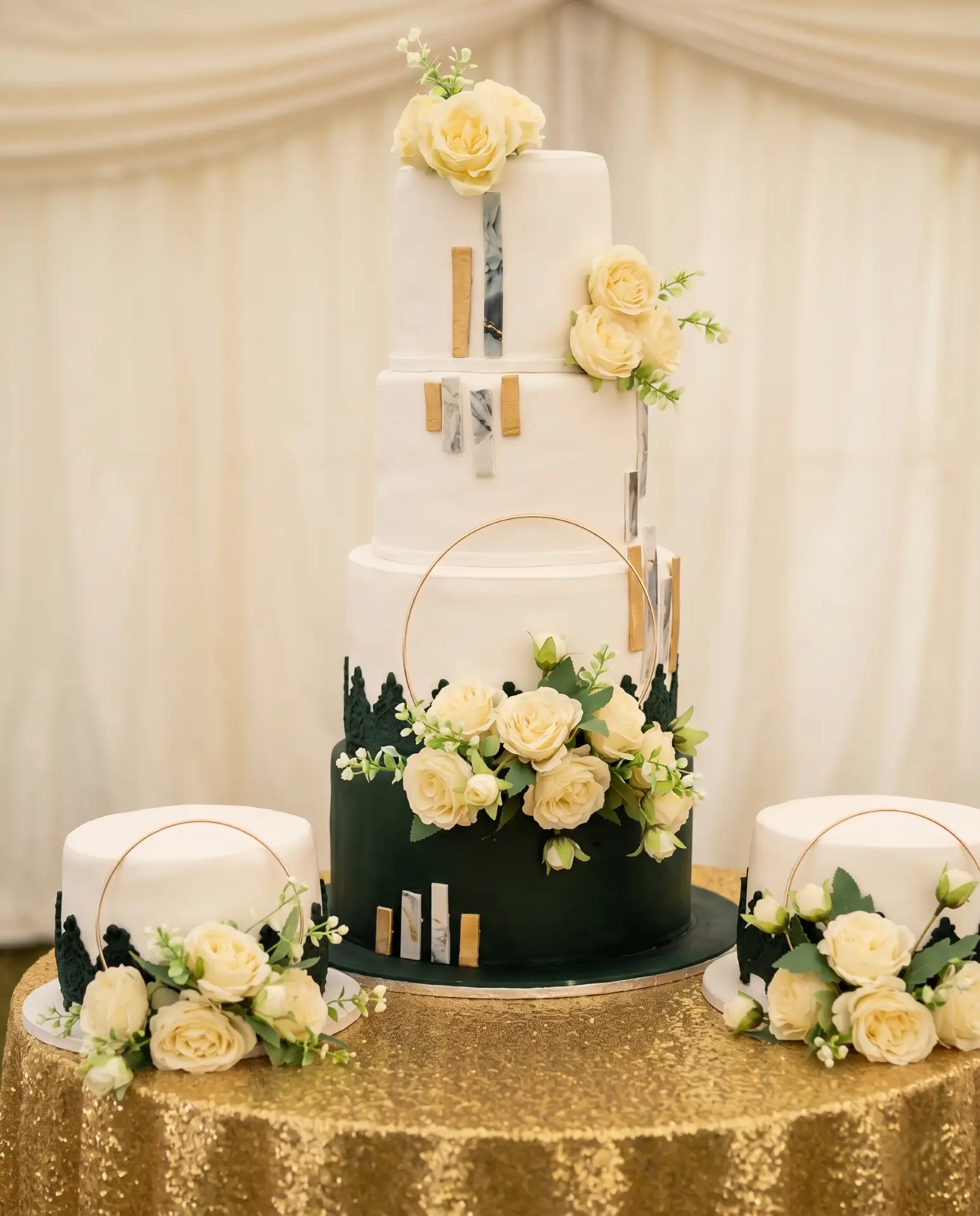 A tall white wedding cake with ivory florals, marble detailing, and gold accents, styled for a traditional rich-fruit wedding stack